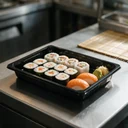 Plateau à sushi 190 × 133 mm en PET noir garni de makis et de california rolls, en cuisine japonaise