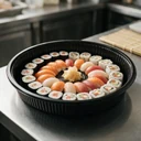 Plateau à sushi rond Ø 330 mm en polystyrène noir garni de sushis en cercles concentriques, en cuisine japonaise