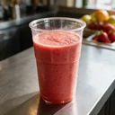 Gobelet PET cristal 40 cl rempli d'un smoothie fraise sur un comptoir de bar à jus