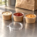 Trois pots kraft fermés, sauces visibles au travers du couvercle, et un couvercle seul